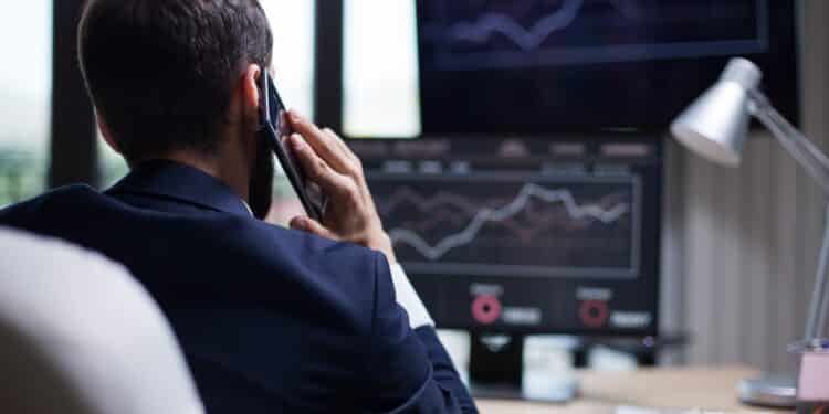 Back view of young business bearded man having a phone call with his CEO. Diagrams on computer monitor.